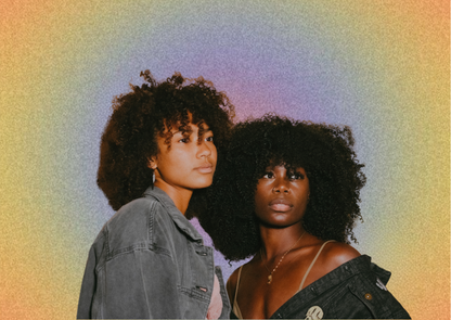 Two women with voluminous dark curly hair pose closely together against a textured, iridescent yellow-to-purple gradient background. The woman on the left wears a faded denim jacket, while the woman on the right wears a dark denim off-shoulder top.