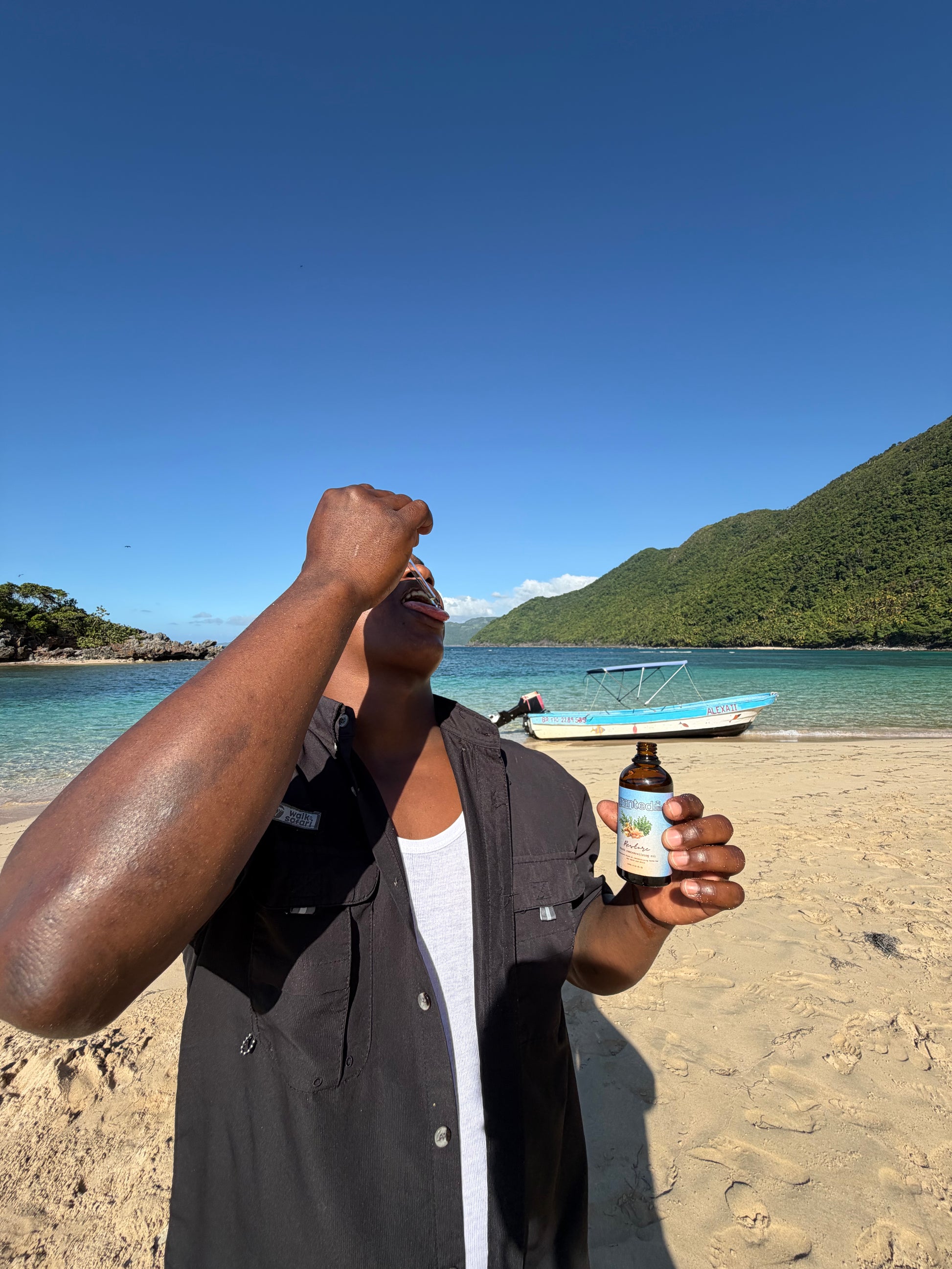 Person holding a bottle on a beach with clear blue sky and water.